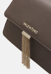 Borsa a mano in pelle marrone con un design strutturato, caratterizzata da una nappina in catena metallica dorata e dal logo "VALENTINO" stampato sul davanti. Texture liscia.