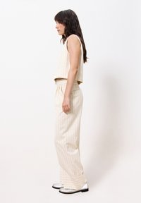 Beige, striped cropped top and matching wide-leg pants in a lightweight fabric, paired with silver-accented shoes. Side view presented.