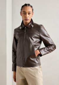 Brun læder zip-up jakke med spidse kraver, sidelommer og en glat tekstur, parret med lyse bukser.