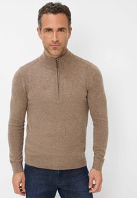 Brauner Zip-Pullover aus strukturiertem Stoff mit hohem Kragen. Verfügt über lange Ärmel und eine taillierte Passform, kombiniert mit dunklen Jeans.