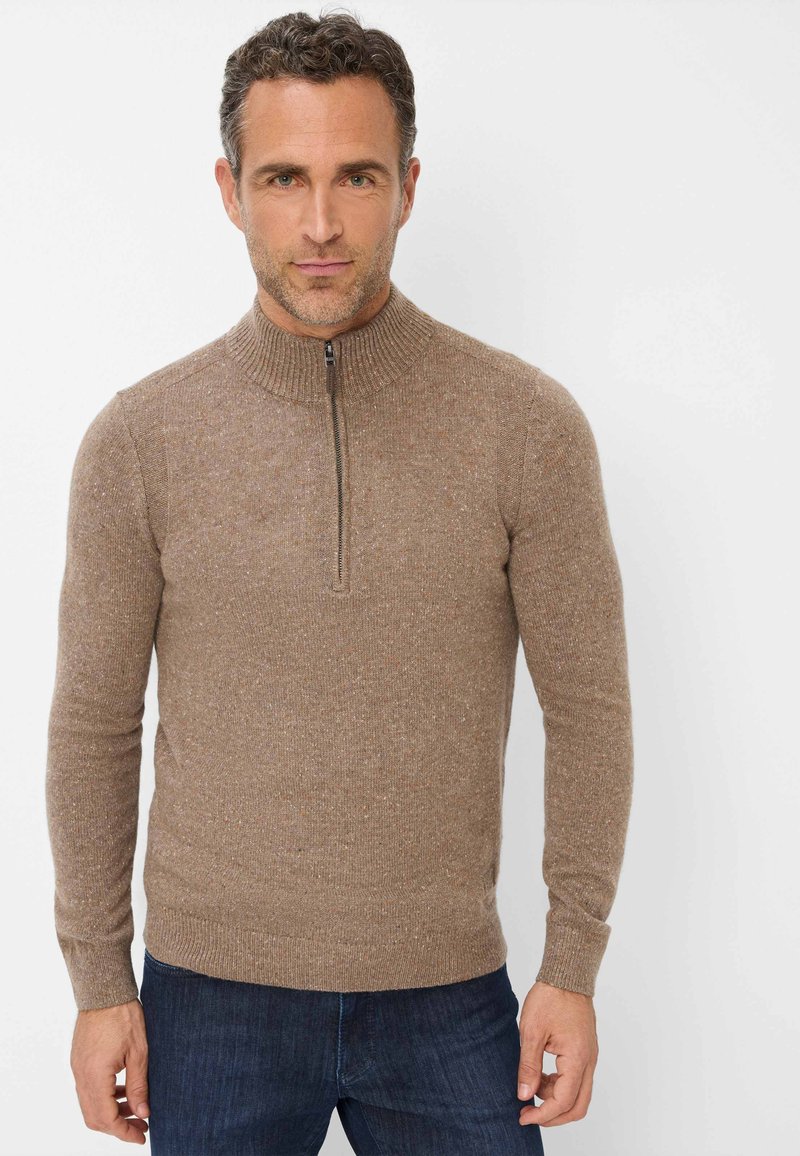 Brauner Zip-Pullover aus strukturiertem Stoff mit hohem Kragen. Verfügt über lange Ärmel und eine taillierte Passform, kombiniert mit dunklen Jeans.