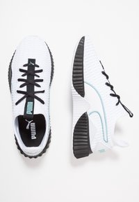 Scarpe da ginnastica bianche in tessuto con una parte superiore testurizzata, lacci neri e suola in gomma. Accenti blu chiaro lungo il lato e dettaglio sulla linguetta.
