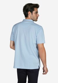 Lichtblauwe polo met korte mouwen, een rechte zoom en zijsplitten. Gemaakt van een gladde stof met een kraag en minimale naden.