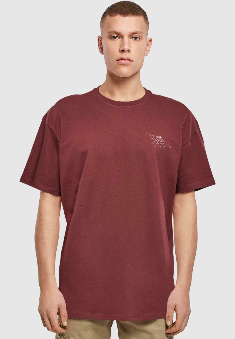 Bordeaux kortærmet T-shirt lavet af bomuld, med et hvidt edderkoppedesign på venstre brystområde. Løs pasform og rund hals.