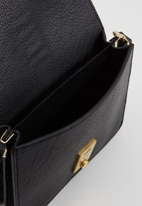 Borsa a tracolla in pelle nera con texture, chiusura magnetica, dotata di una clasp dorata e di un ampio interno dal design elegante e semplice.