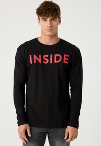 Camiseta de manga larga negra hecha de algodón, con el texto rojo en negrita "INSIDE" en el pecho. Diseño sencillo de cuello redondo, ajuste casual.