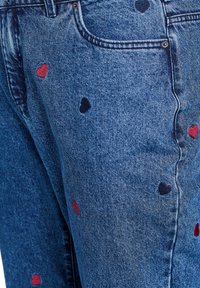 Jeans de denim con un acabado azul clásico, que presentan pequeños bordados en forma de corazón rojo y negro esparcidos por la tela.