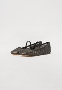 Ballerines noires tissées avec un bout pointu, des côtés ouverts et deux lanières élastiques. Surface texturée avec un motif subtil et une semelle plate.