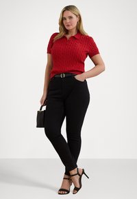 Rød kortermet kabelstrikket polo-skjorte, svarte høytaljede jeans og svarte stropphevede sandaler. Har en liten håndveske.