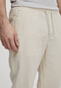 Pantalones jogger de lino color beige claro con cintura elástica y cordón ajustable. Cuentan con bolsillos laterales y tela suave y texturizada.