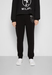 Schwarze Sweatpants aus weichem Stoff, mit lockerer Passform und gerippten Bündchen, verziert mit einem Bärenmotiv in glänzenden Akzenten an der Seite.