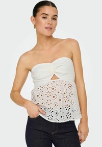Top bianco senza spalline con scollatura testurizzata e motivo in pizzo floreale sull'orlo. Abbinato a jeans blu scuro.