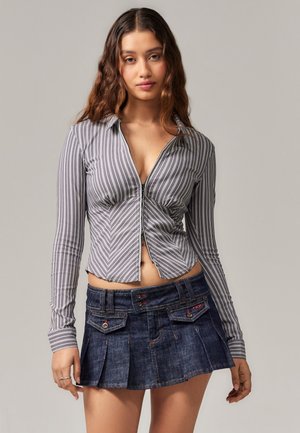 Camisa de manga larga a rayas en gris con líneas verticales blancas, cierre con cremallera; combinada con una falda mini de mezclilla con bolsillos y detalles coloridos.
