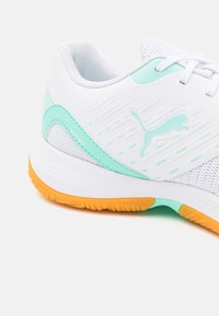 Hvit idrettssko med mesh-detaljer, mintgrønn pynt, teksturert oransje såle og en Puma-logo på siden.