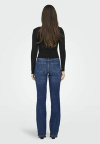 Jeans in denim blu con un design a gamba svasata, dotati di tasche posteriori standard e vita media, abbinati a una maglietta nera a maniche lunghe.