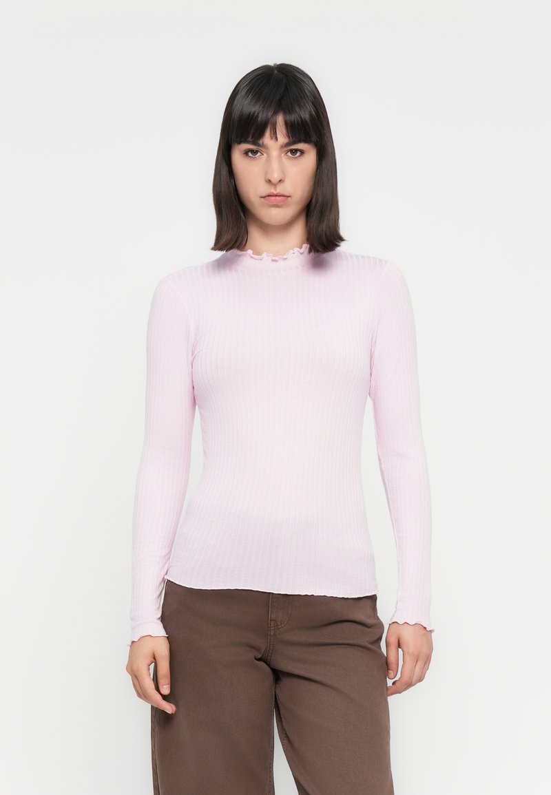 Lichtroze geribbelde longsleeve top met een golvende halslijn en een strakke pasvorm, gecombineerd met bruine broek.