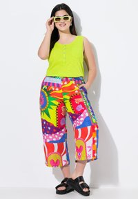 Top senza maniche di un vivace verde brillante con tasca e dettaglio dei bottoni, abbinato a pantaloni a gamba larga con un motivo colorato. Sandali con plateau neri completano il look.