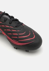 Botín de fútbol negro con detalles rojos, textura suave, diseño ligero y múltiples tacos en la suela para tracción. Cuenta con un cierre de cordones.