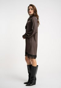 Brązowa satynowa sukienka z długimi rękawami, z detalem koronkowego wykończenia na dole. Połączona z czarnymi, sięgającymi do kolan botkami na koturnie. Prosty kołnierzyk.