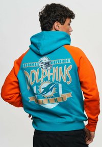 Hoodie med turkos kropp och orange ärmar. Har texten "DOLPHINS" och en logotypgrafik på baksidan, tillsammans med detalj av en banner med "Miami".