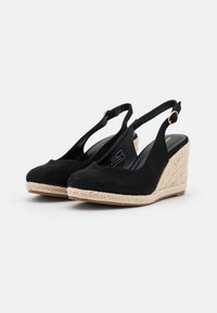 Čierne semišové platformové sandále so slingback dizajnom, tkanou jutovou podrážkou a okrúhlou špičkou. Obsahuje kovovú pracku na popruhu.