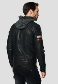 Černá kožená bunda s džínovou kapucí, prošitými detaily na ramenech a kontrastními červenými, bílými a šedými pruhy na rukávech.