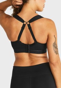 Zwarte sportbeha met een netstof, brede banden en een haaksluiting op de rug, met een logo op de band.