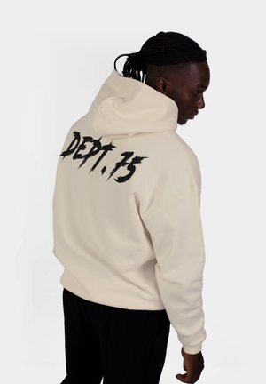 Felpa color crema con una grande grafica nera "DEPT.13" sul retro. Presenta una vestibilità comoda e un cappuccio. Il tessuto sembra morbido.