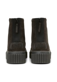 Une paire de bottes de cheville en daim marron foncé avec des fermetures éclair noires et des semelles en caoutchouc épaisses et texturées, vues de l'arrière.