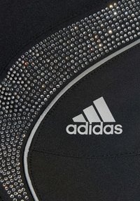Čierna športová tkanina so strieborným logom Adidas; ozdobená vzorom jasných rhinestones po okraji pre dekoratívny detail.