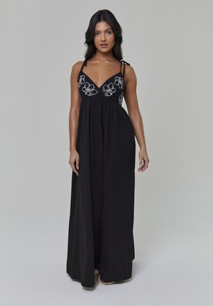 Schwarzes Maxi-Kleid mit floraler Stickerei am Dekolleté, verstellbaren Trägern zum Binden, fließender Silhouette und weicher Stoffstruktur.