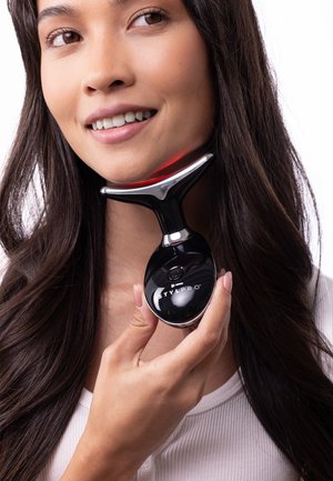 Zwart handheld apparaat met een glanzend zilveren accent, met een afgeronde rand en een rood licht, dicht bij de kaaklijn van een persoon gehouden.