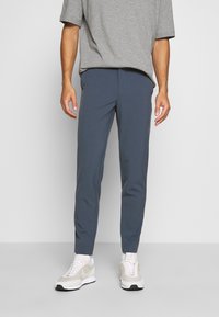 Šedé oversized tričko v kombinaci s tmavě modrými tapered kalhotami. Kalhoty mají hladkou texturu a jednoduchý design bez viditelných vzorů.