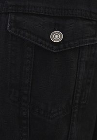 Chaqueta de mezclilla negra con un bolsillo en el pecho en punta, cierre de botones a presión plateados y detalles de costura en contraste. Diseño clásico.