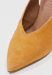 Gros plan sur une chaussure plate en daim jaune moutarde à bout pointu avec des coutures visibles et une doublure intérieure texturée.