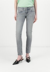Sive jeans skinny iz petimi žepi, zbledela tekstura in gumbasto zapiranje. V kombinaciji s črnimi lakastimi čevlji s konicami.