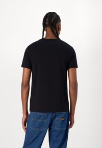 Sort kortærmet t-shirt lavet af bomuld, med rund hals og lige snit, båret sammen med blå denimbukser med baglomme.