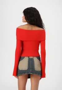 Top rosso a coste, senza spalline e con maniche lunghe, abbinato a una gonna di jeans con tasche beige e orlo grezzo.