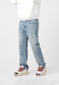 Light blue denim jeans with a relaxed fit, featuring front pockets and subtle fading. Paired with white and grey sneakers with colored laces.