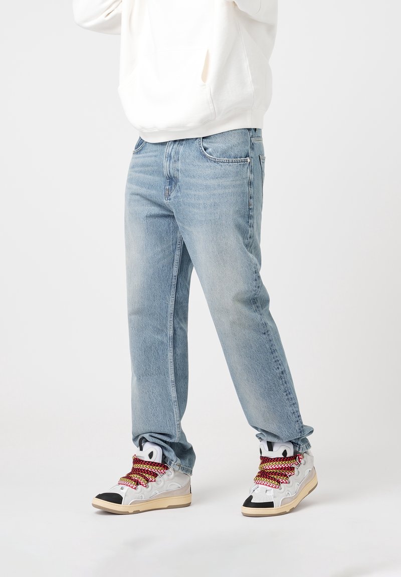 Light blue denim jeans with a relaxed fit, featuring front pockets and subtle fading. Paired with white and grey sneakers with colored laces.