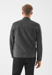 Giacca in suede grigia con una texture morbida, design minimalista e collo piatto. Presenta dettagli cuciti e una vestibilità sartoriale.