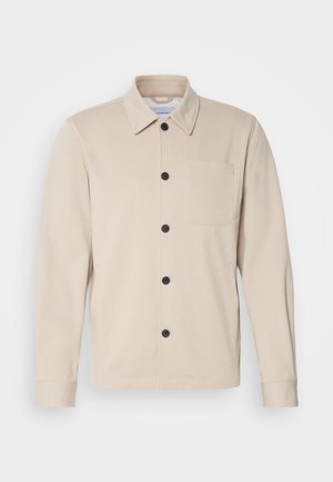 Smėlio spalvos mygtukinė striukė iš minkštos medžiagos, turi apykaklę, priekinius kišenių ir juodus mygtukus. Ilgos rankovės su siuvinėtėmis antkrakčių.