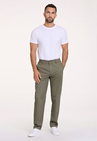 Zielone spodnie o prostym kroju, wykonane z tkaniny, zestawione z dopasowaną białą koszulką i białymi sneakersami. Prosty design i neutralne kolory.