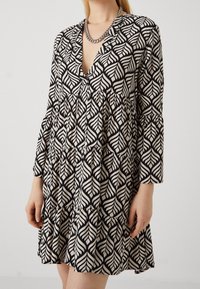 Vestido de patrones de hojas en negro y beige con escote en V, mangas largas y diseño de volantes en capas. Hecho de una tela ligera.