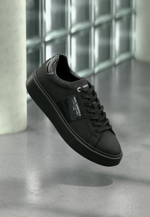 Black sneakers with smooth leather upper, round toe, and thick rubber sole. Features a glossy panel and lace-up design.