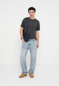 Γκρι μπλουζάκι, ανοιχτό μπλε χαλαρό τζιν και ταμπά αθλητικά παπούτσια. Το μοντέλο κρατά μια μικρή σκούρα μπλε τσάντα από τζιν με καφέ λεπτομέρειες. Απλό και καθημερινό στυλ.