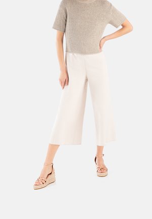 Top corto a maniche corte in maglia beige, pantaloni bianchi larghi e cropped, e zeppe in tela rosa chiaro con cinturini intrecciati e lacci alla caviglia.