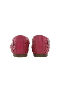 Zapatos de cuero rosa con detalles trenzados en la parte trasera, suela plana y un pequeño acento metálico cerca del talón.