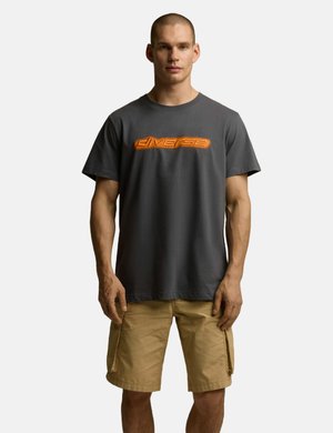 Szara bawełniana koszulka z pomarańczową grafiką "diverse" na wysokości klatki piersiowej, w połączeniu z beżowymi szortami cargo. Prosty okrągły dekolt, luźny krój.