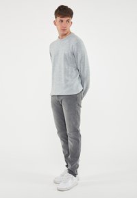 Maglione grigio chiaro con collo rotondo, abbinato a jeans slim-fit grigio scuro e sneakers bianche. Il tessuto sembra morbido con una lieve texture.
